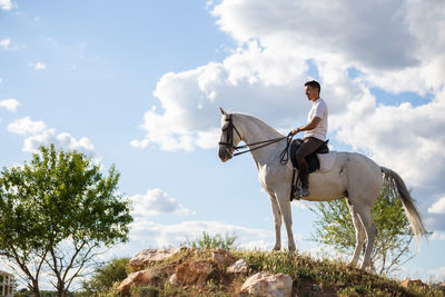 Side view of man riding horse on land against sky