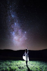 Woman walking on field against sky at night