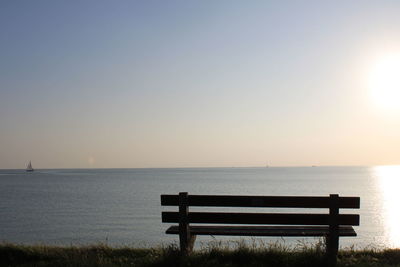 Bench by sea against clear sky during sunset