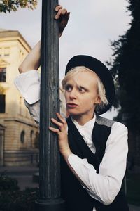 Young woman looking away while standing by pole against trees