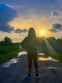 Rear view of woman standing on field against sky during sunset