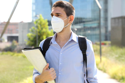 Man looking away while holding files against building