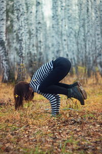 Side view of woman practicing handstand in forest