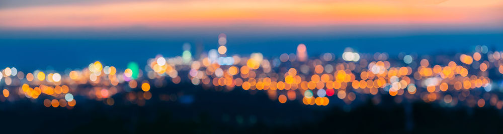 Defocused image of illuminated cityscape against sky at sunset