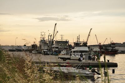 Boats moored at harbor against sky during sunset