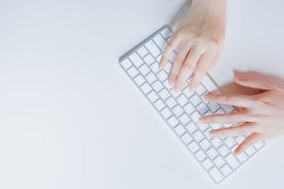 Cropped hands typing on keyboard against white background