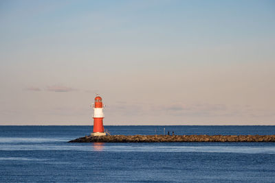 Lighthouse by sea against sky during sunset