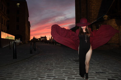 Woman standing on street against sky at sunset