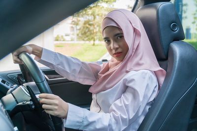 Portrait of young woman in hijab driving car