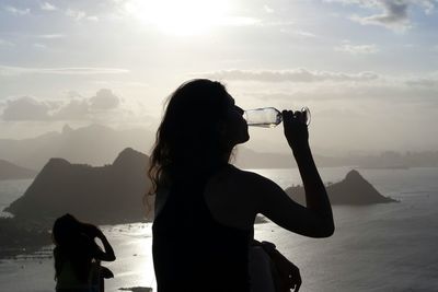 Silhouette two women drinking wine on mountain by sea during sunset