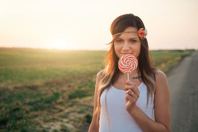 Portrait of smiling young woman holding lollipop with field in background