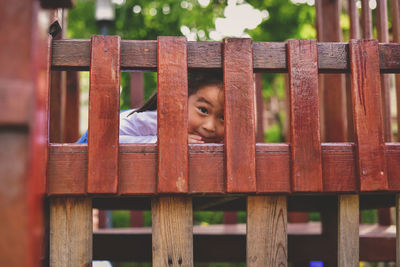 Portrait of girl looking through wooden fence 