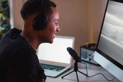 Smiling young freelance worker wearing headphones podcasting in front of computer