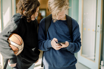 Male students using smart phone in school corridor