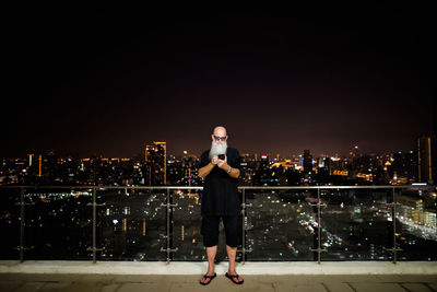 Rear view of man standing against illuminated buildings in city at night