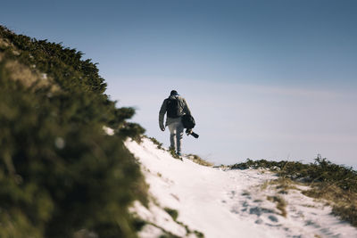 Rear view of man walking on snowcapped mountain against sky