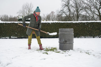 Middle-aged woman is collecting snow in a barrel with a shovel,natural resources