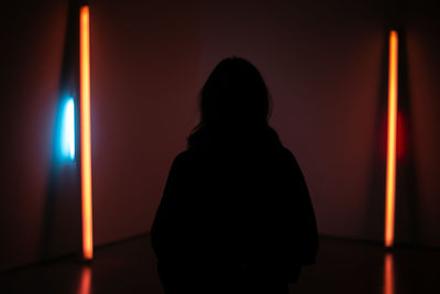 Rear view of silhouette woman standing against illuminated wall