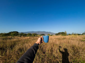 Midsection of man drinking glass on field against clear blue sky