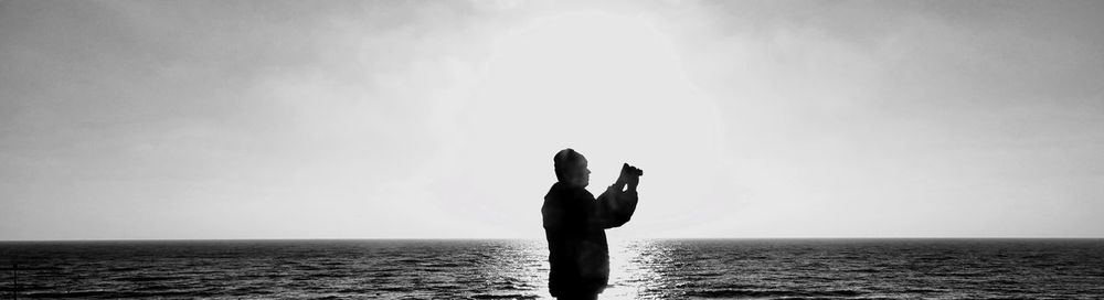 Silhouette man standing at beach against sky