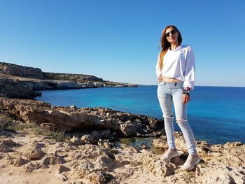 Woman standing on rock by sea against sky