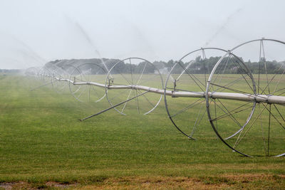 Agricultural sprinkler spraying on grassy field at farm against sky