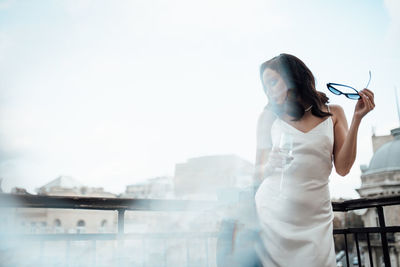 Woman standing on railing against sky