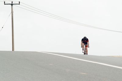 Man riding bicycle on road against clear sky