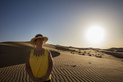 Senior woman standing at desert against clear sky during sunny day