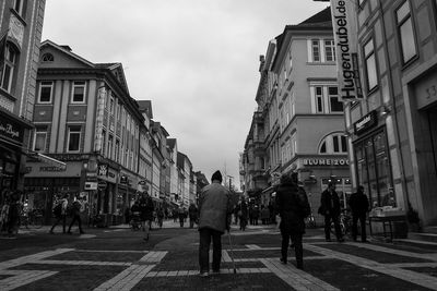 People walking on city street amidst buildings against sky