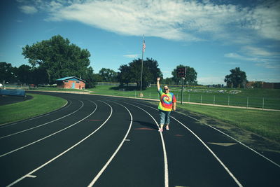 Woman gesturing while standing on running track against sky