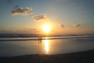 Silhouette people standing on beach against sky during sunset