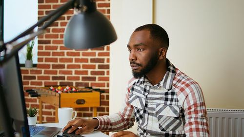 Side view of young man using mobile phone while standing at home