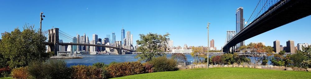 Manhattan bridge and brooklyn bridge over hudson river by buildings against clear sky