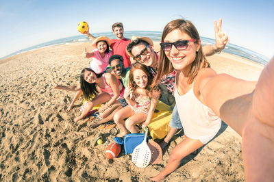 Portrait of smiling young friends taking selfie at beach on sunny day