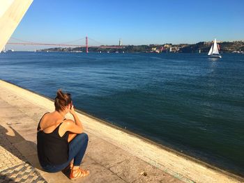 Man sitting on bridge over sea against sky