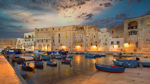 Boats moored in canal amidst buildings against sky at sunset