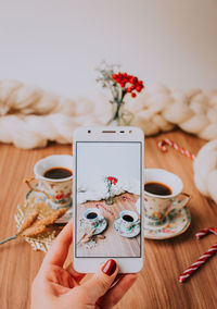 Close-up of hand photographing coffee cups on mobile phone at table