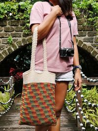 Woman holding bag while standing with camera on bridge