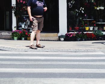 Low section of man standing on sidewalk against flower shop during sunny day