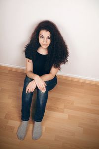 Portrait of woman sitting on hardwood floor against wall at home