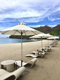 Lounge chairs and parasols on beach against sky