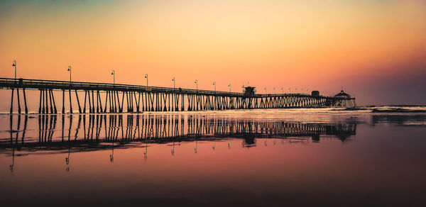 Silhouette pier on sea against orange sky