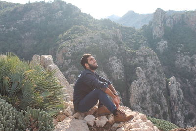 Young man sitting on rock against mountains