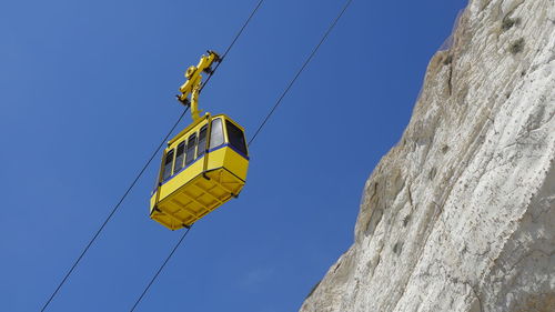 Yellow funicular car against the background of the sky and white rock