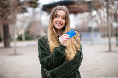 Portrait of woman holding credit card while standing in park