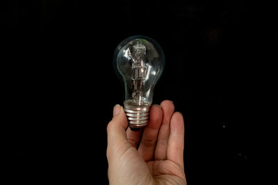 Close-up of hand holding light bulb against black background