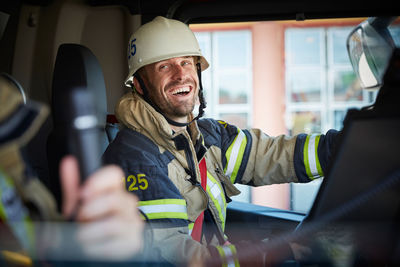 Smiling firefighter looking at coworker while sitting in fire engine