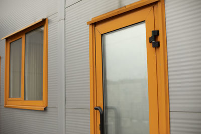 Orange door to building. entrance to office. door with glass. grey house panel.