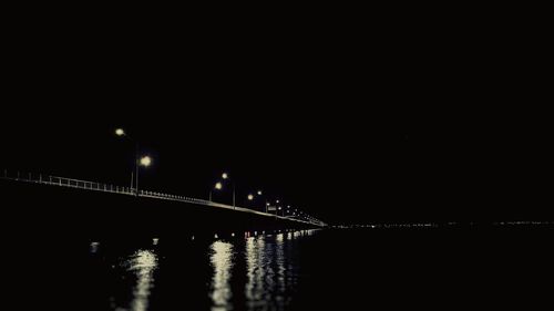 Illuminated bridge over river against sky at night